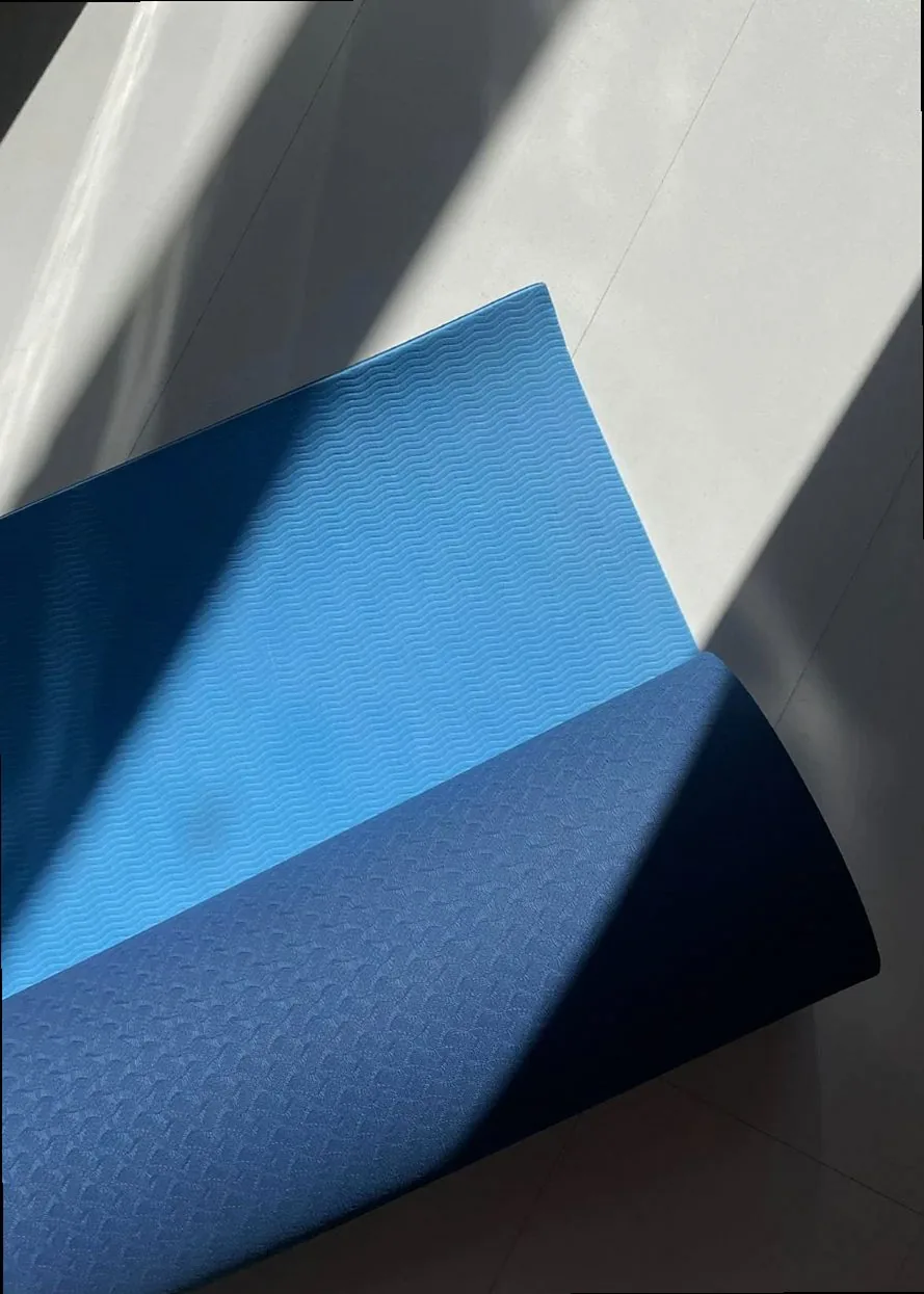 A blue yoga mat partially rolled out on a sunny floor, casting shadows and light patterns.