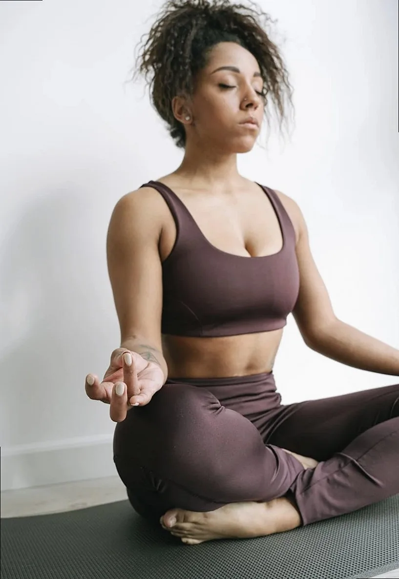 An adult woman in activewear practicing meditation in lotus pose indoors, promoting mindfulness and relaxation.